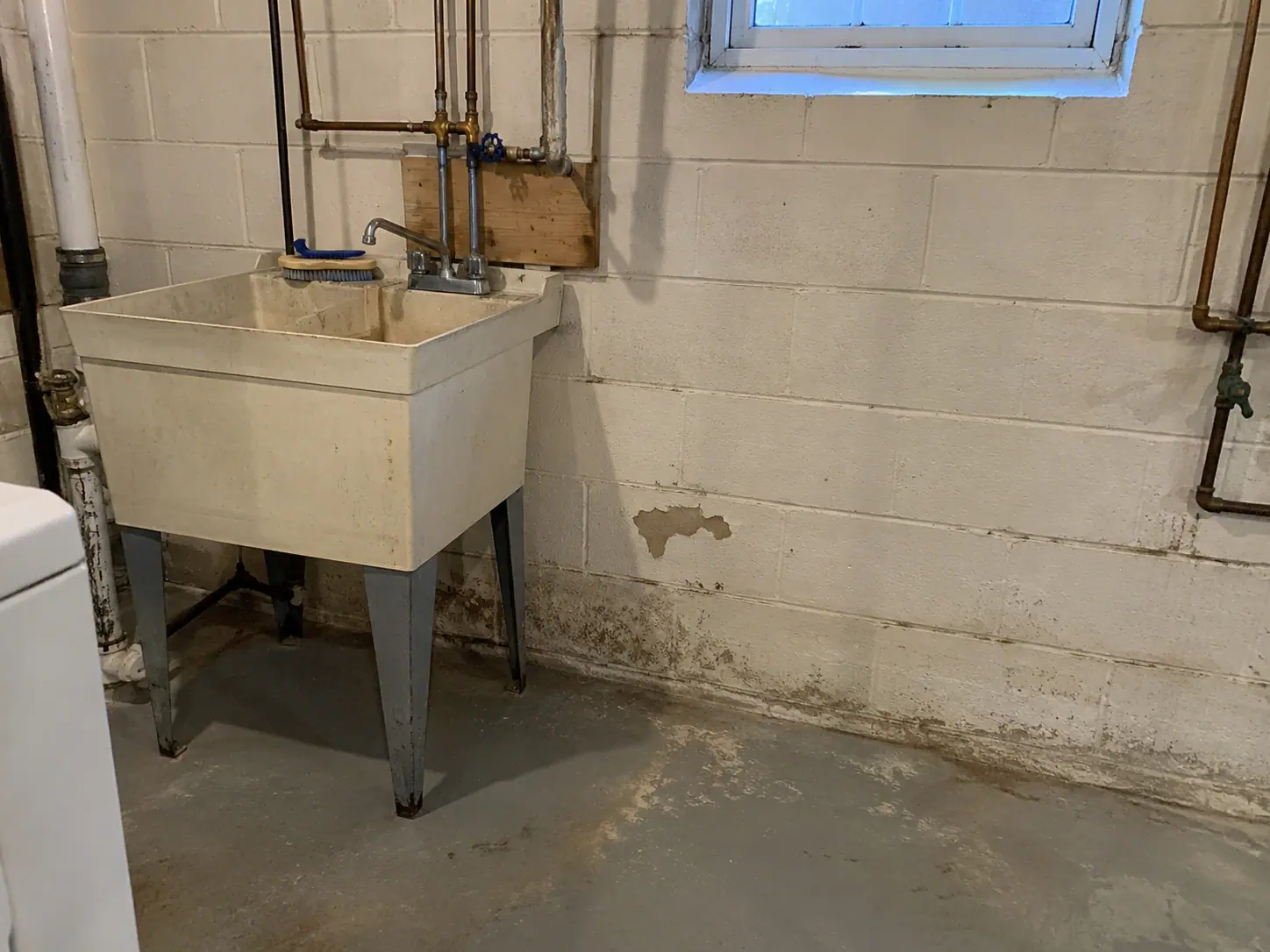 Unfinished basement wall with peeling paint and moisture staining near the floor